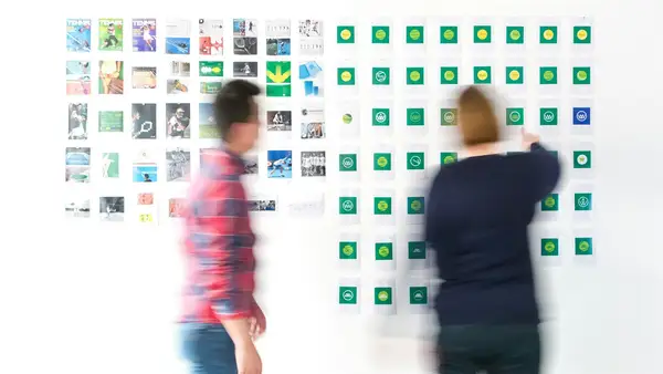 Dos personas analizando una pared llena de logotipos y referencias visuales de marca