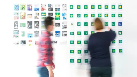 Dos personas analizando una pared llena de logotipos y referencias visuales de marca